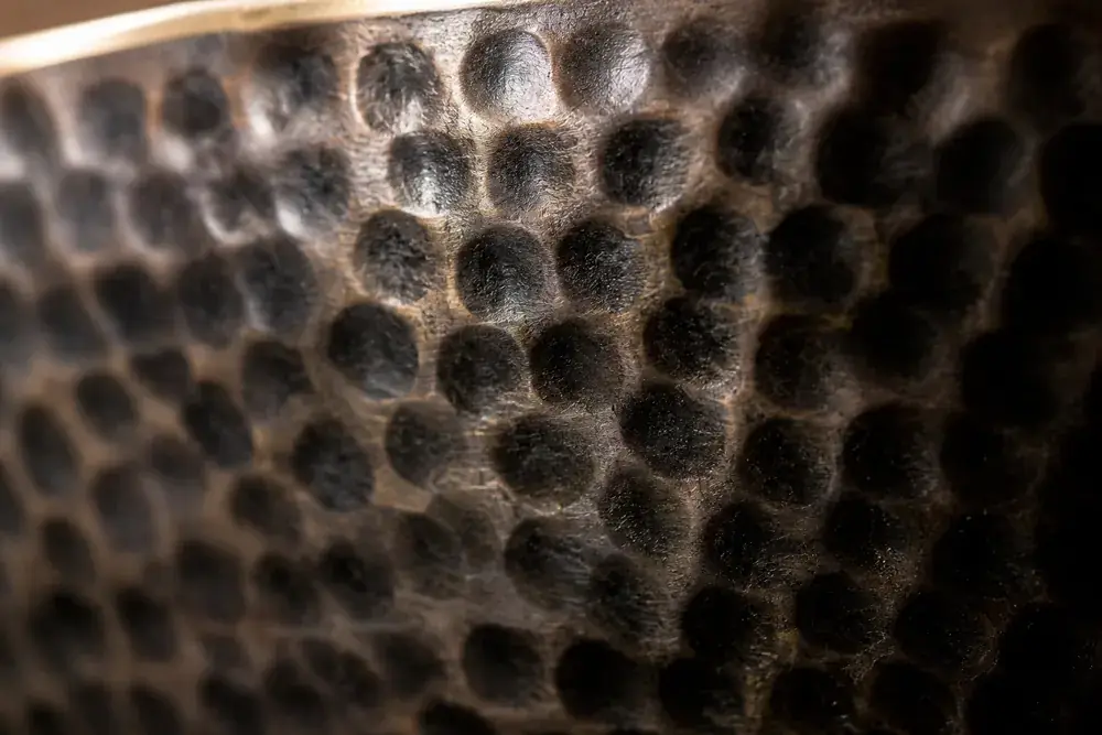 Extreme close-up of the dimpled hammer marks covering the wall of a darkened bronze singing bowl