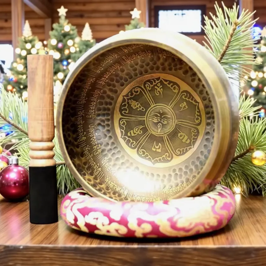 Verified buyer photo: large dark engraved bronze singing bowl on a pink cushion with its mallet standing beside it, festive greenery in the background