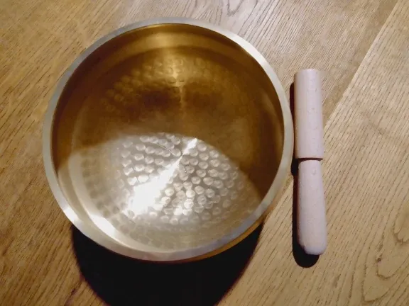 Verified buyer photo: brass singing bowl next to its light wooden mallet on a warm wood floor